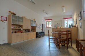 Una cuina àmplia amb armaris de fusta, una zona de menjador amb cadires i taula, i una finestra amb cortines vermelles.