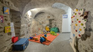 A room with stone walls, a red carpet, and various children's toys and decorations. - Il Seicento - Hostel (Sernio)