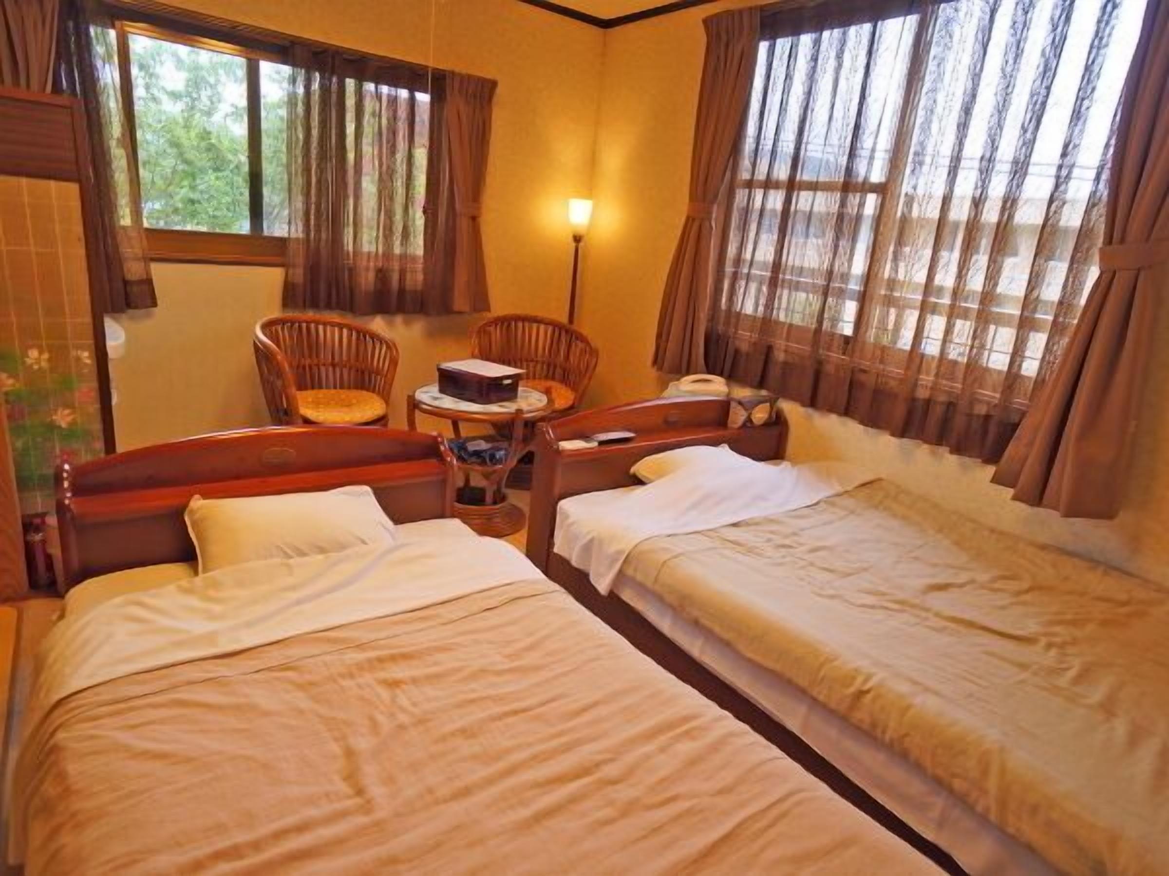 A room with two beds, a small table, a chair, and a lamp.