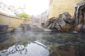 Une zone de sources chaudes avec de l’eau claire, des rochers et une clôture en bambou.