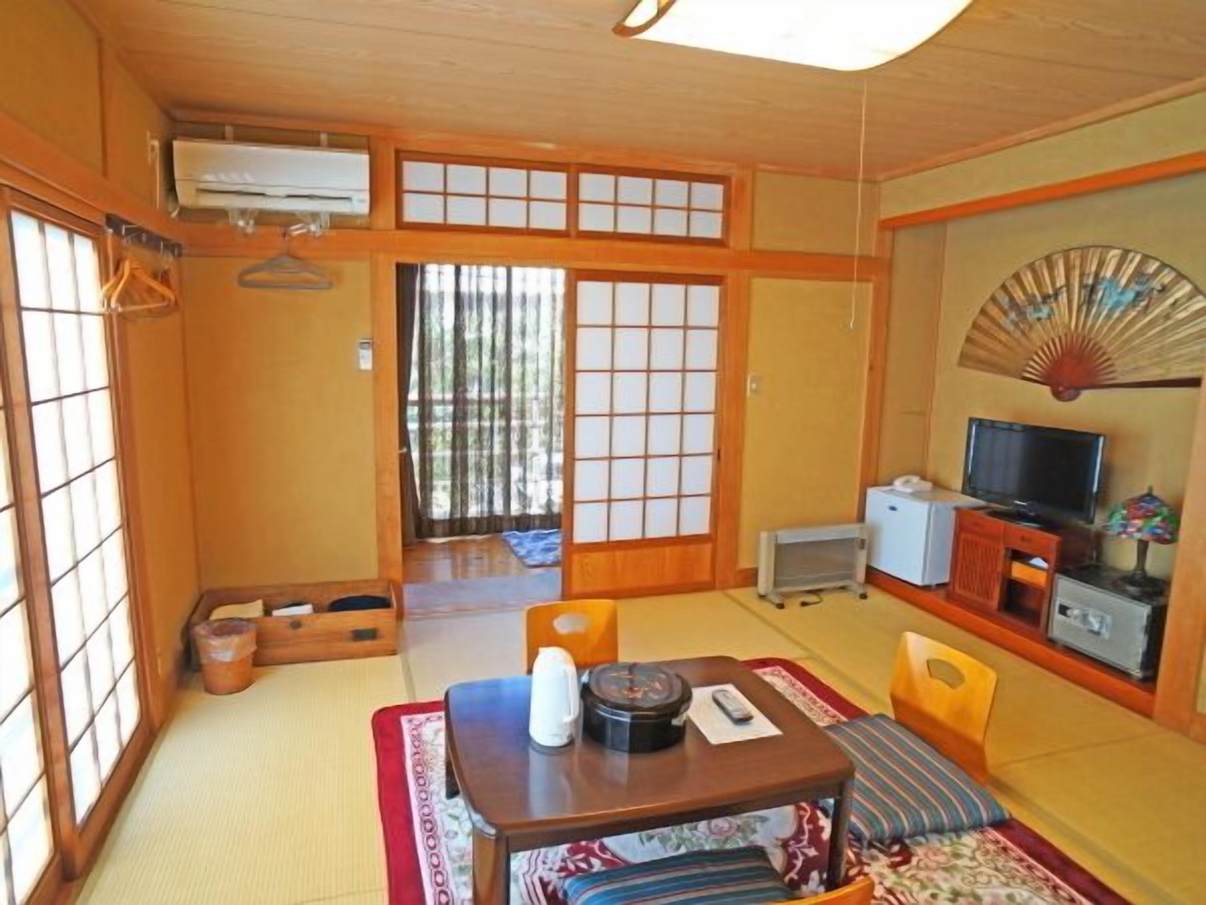 A traditional Japanese room with tatami flooring, a low table with a kettle, a television, and a fan on the wall.