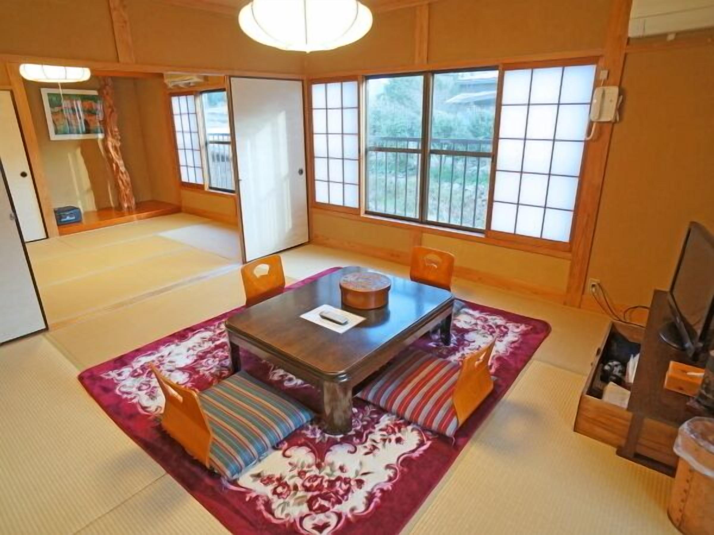 A traditional Japanese room with tatami flooring, a low table, cushions, and sliding doors.