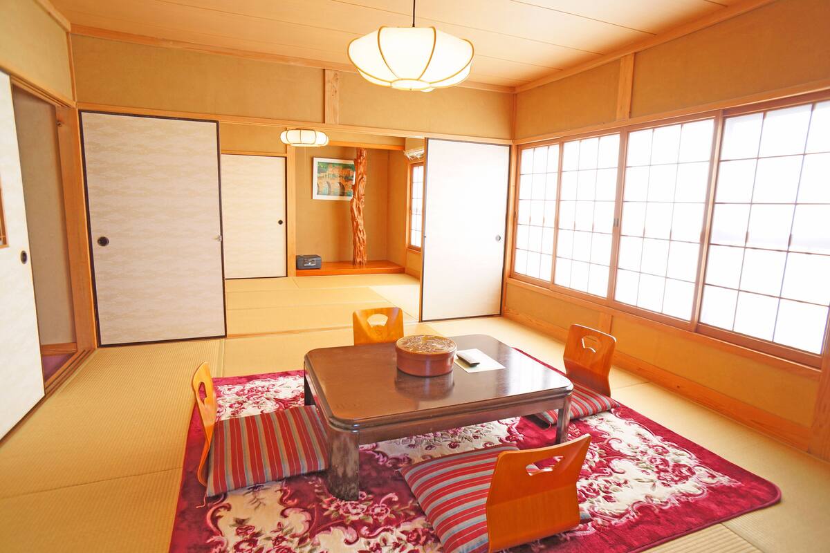 Een traditionele Japanse kamer met tatami vloerbedekking, een lage tafel met kussens en schuifdeuren.