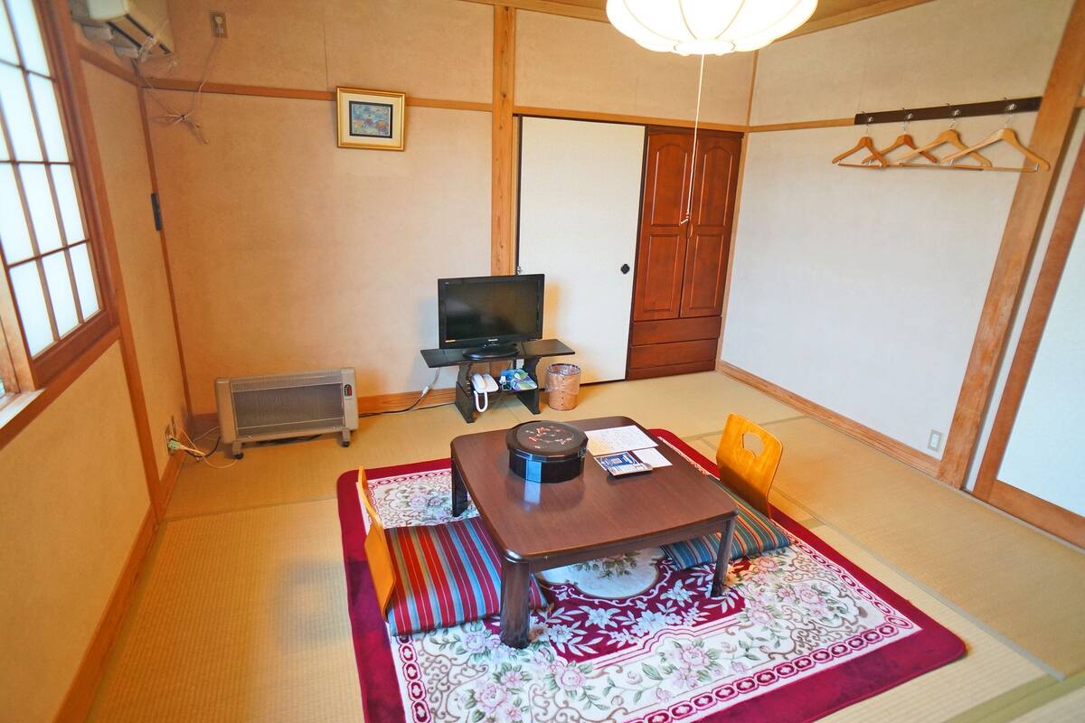 Een traditionele Japanse kamer met tatami vloerbedekking, een lage tafel met kussens, een televisie en een verwarming.
