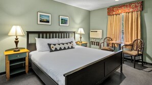 A hotel room with a bed, two bedside lamps, a nightstand, a table with chairs, and a window with curtains. - Old Town Inn (Crested Butte)