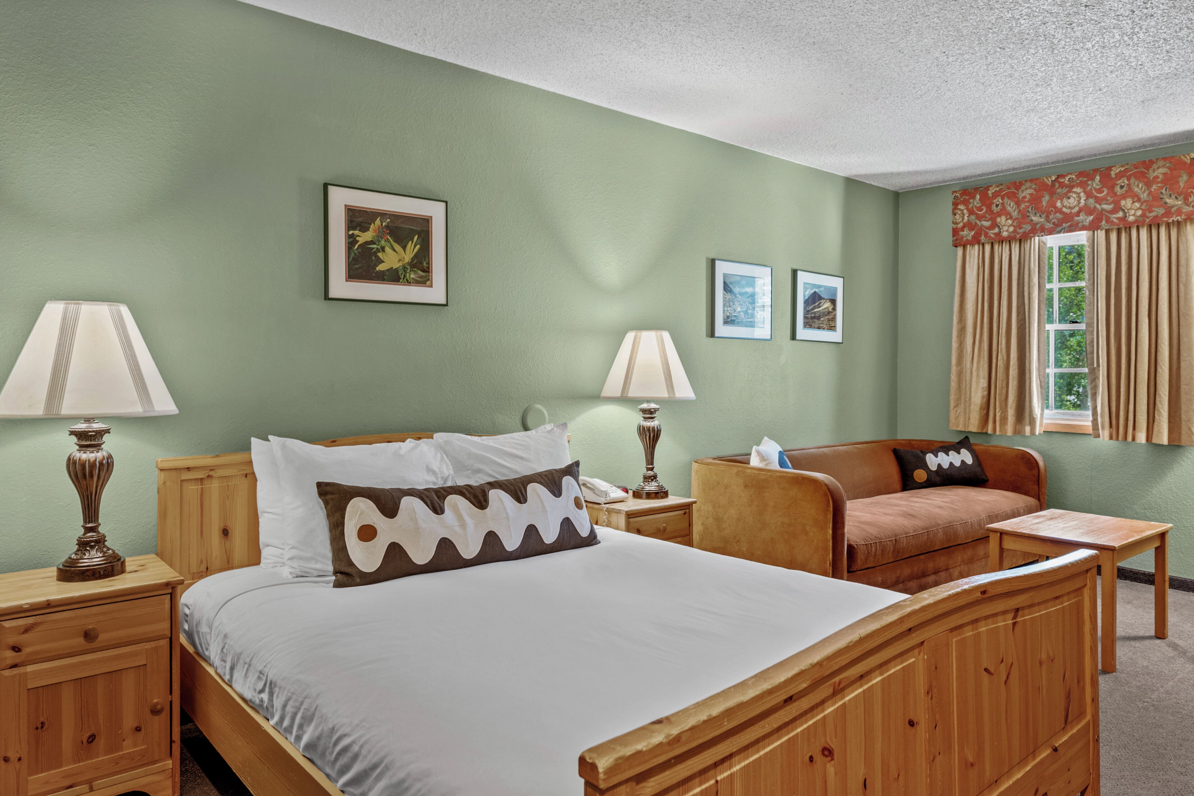 Una habitación con cama, dos mesitas de noche con lámparas, un sofá y una ventana con cortinas.