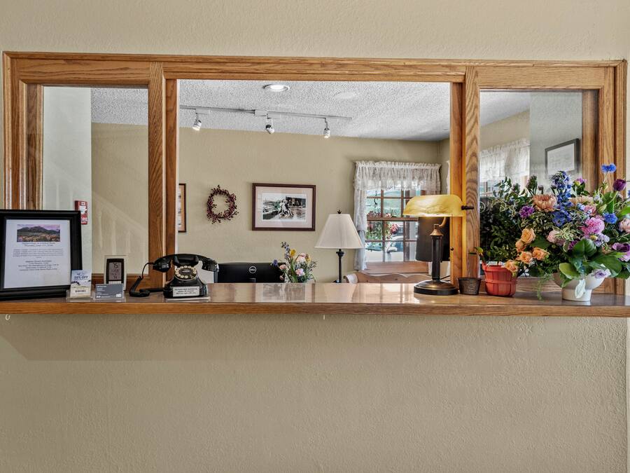 Ein Empfangsschalter mit Spiegel, gerahmten Bildern, einem Telefon, einer Lampe und einer Blumenvase.