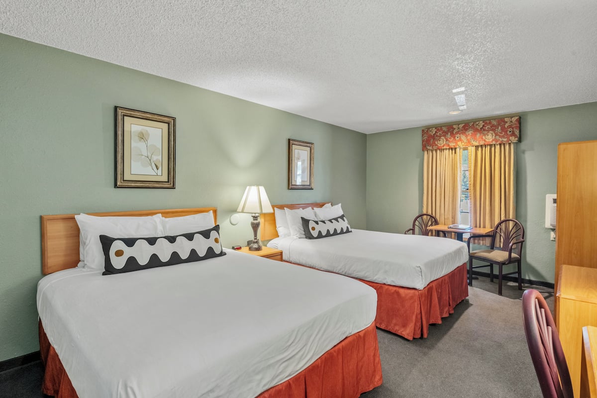 A hotel room with two beds, a desk, a chair, and a window with curtains.