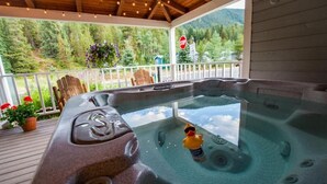 Un jacuzzi con un flotador de pato, rodeado por una terraza de madera, con vista a un área boscosa y una señal de stop al fondo.