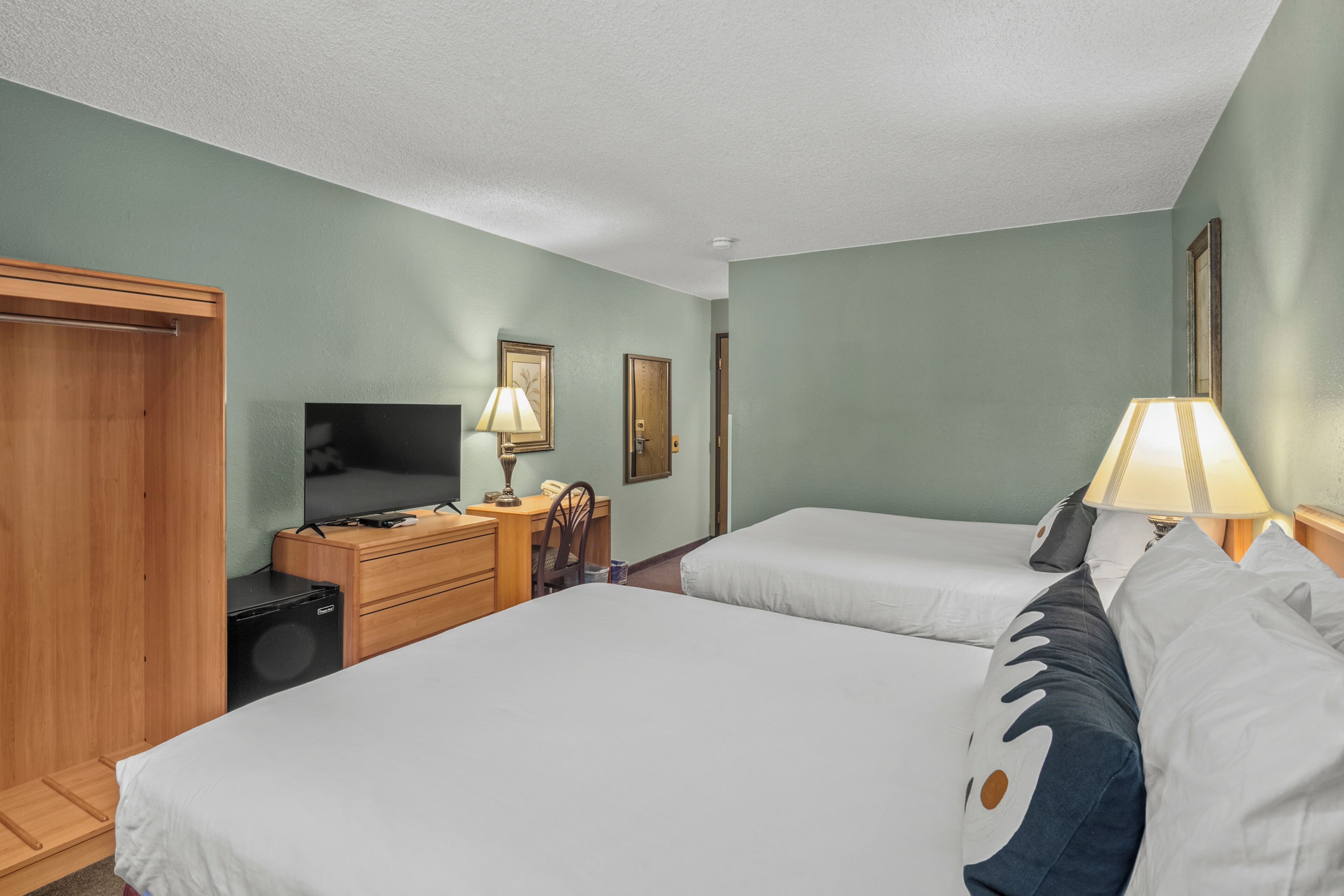 A hotel room with two beds, a desk, a television, a lamp, and a wardrobe.