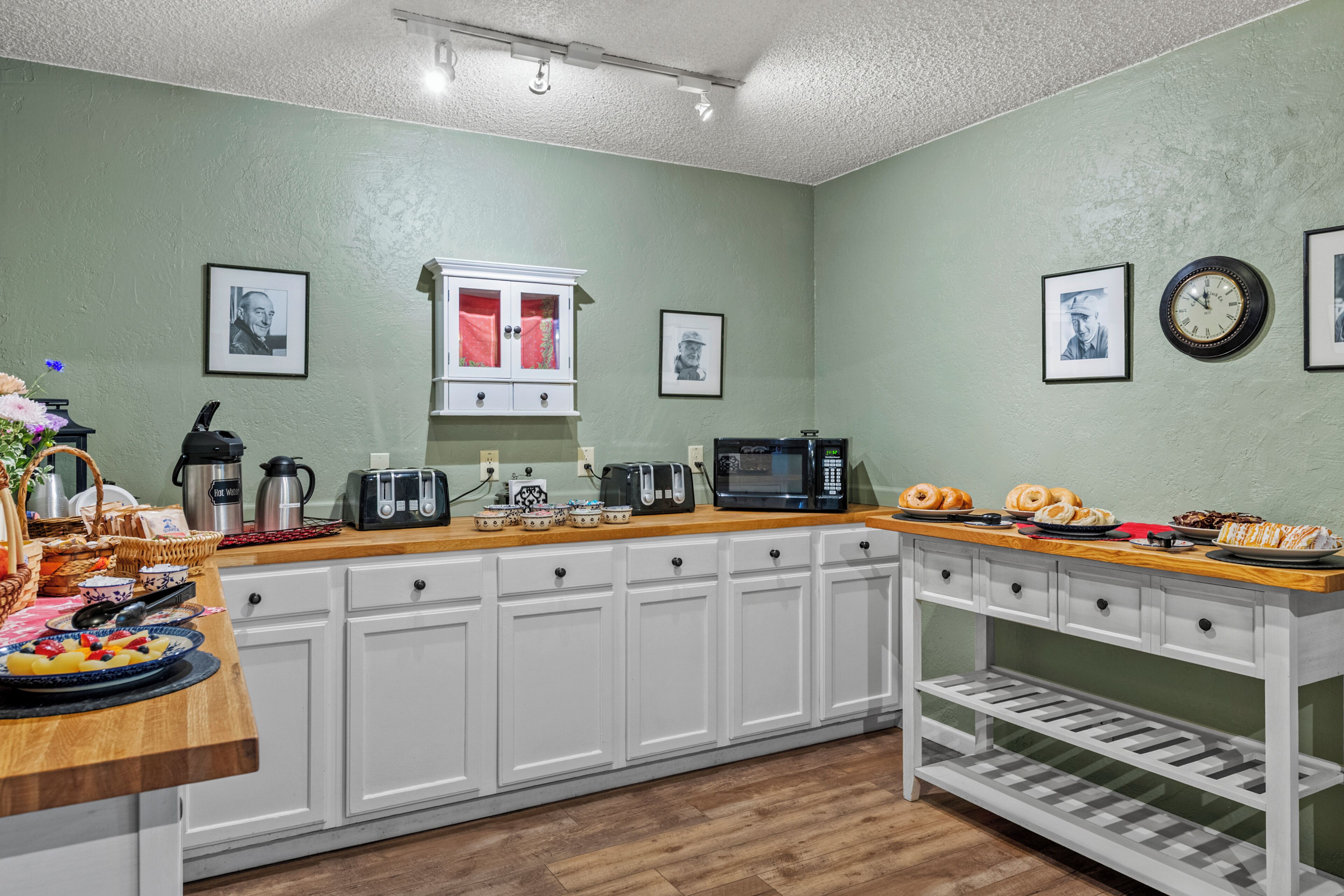 A kitchen with white cabinets, a wooden countertop, a coffee maker, a toaster, and a clock on the wall.