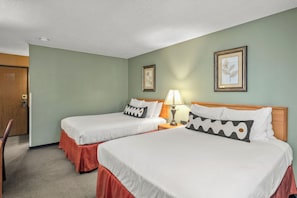 A hotel room with two beds, a wooden door, a framed picture on the wall, and a lamp on the nightstand. - Old Town Inn (Crested Butte)