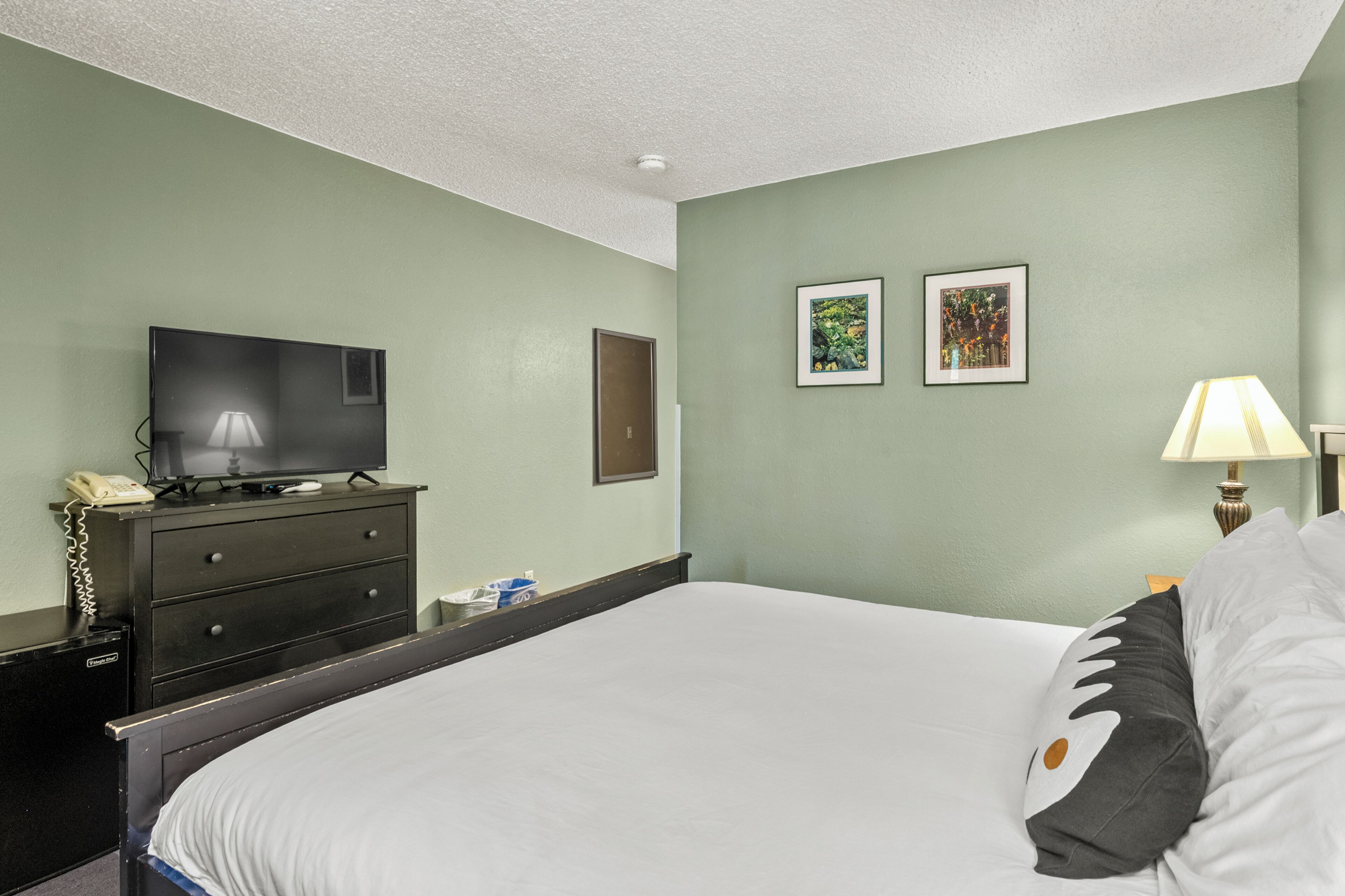 A hotel room with a bed, a television on a dresser, a lamp, and two framed pictures on the wall.