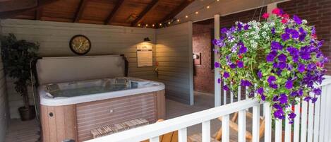 A hot tub on a wooden deck with a brick wall and a hanging flower basket.