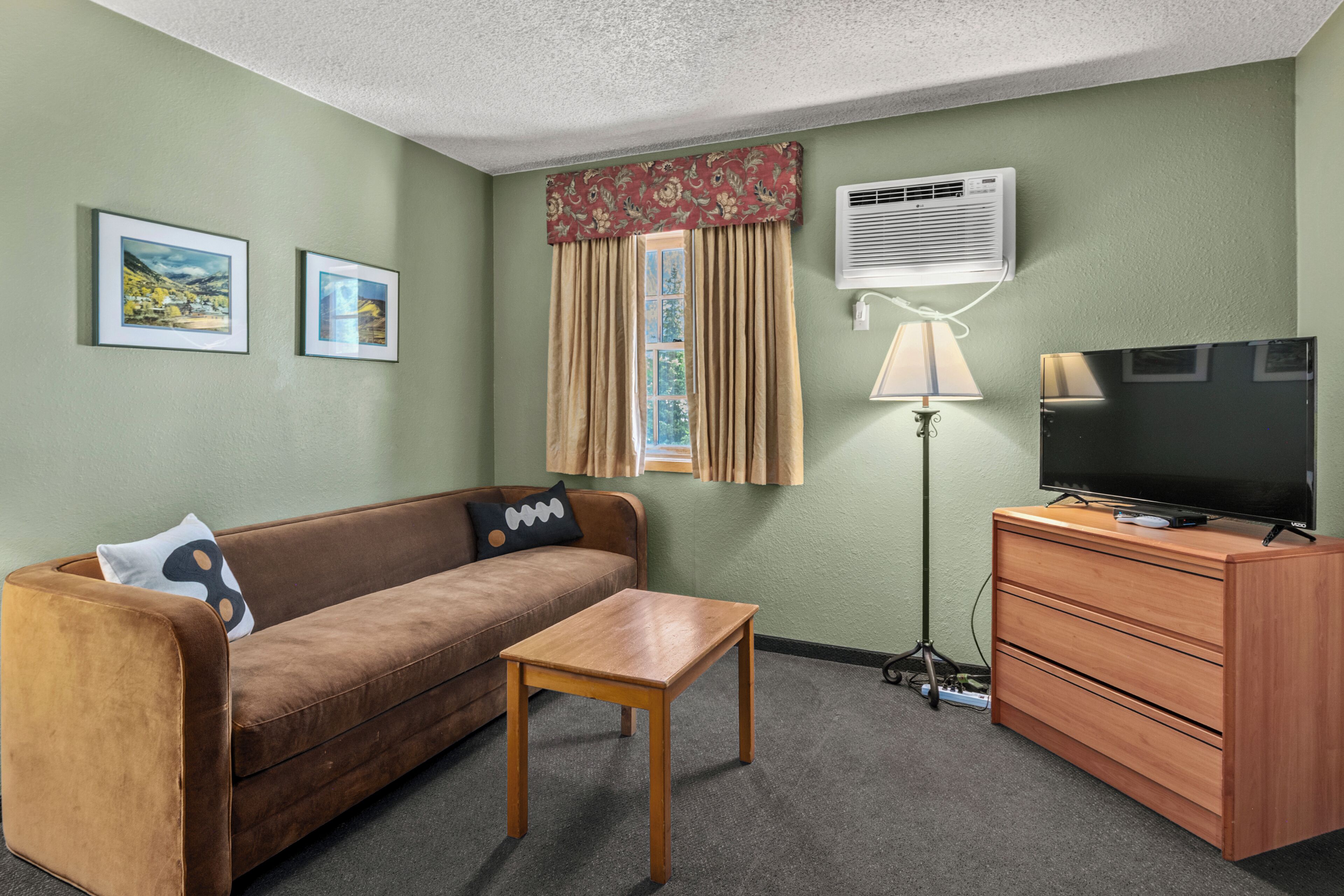 A living room with a sofa, a coffee table, a TV on a wooden cabinet, a lamp, and framed pictures on the wall.