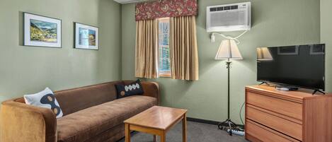 A living room with a sofa, a coffee table, a TV on a wooden cabinet, a lamp, and framed pictures on the wall.