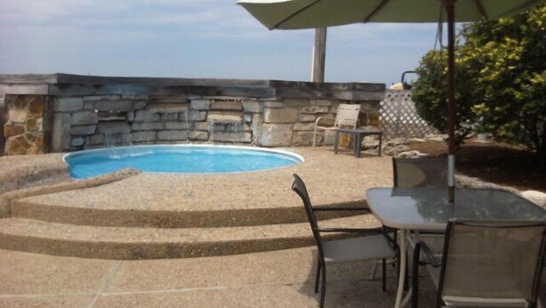 Una piscina con muros de piedra, un patio con sillas y una mesa.