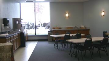 A conference room with a large table and chairs, a kitchenette, and a view through a large window.