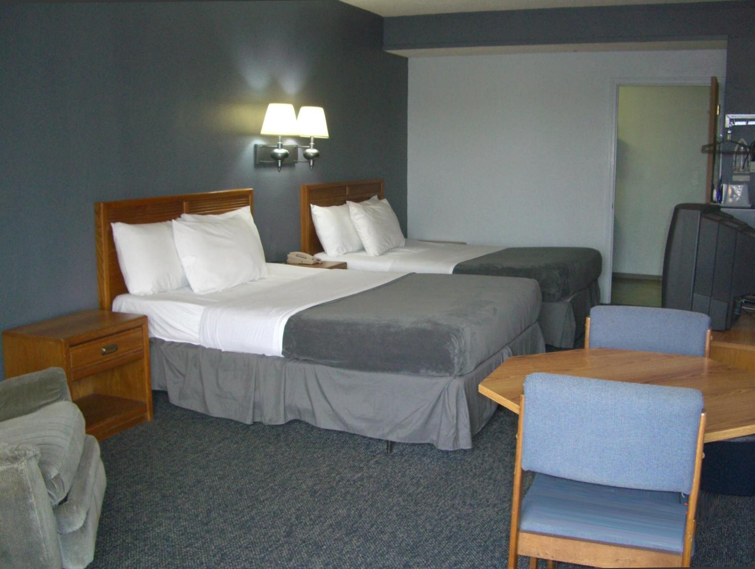 Une chambre d’hôtel avec deux lits, un bureau, une chaise, une télévision et une lampe.