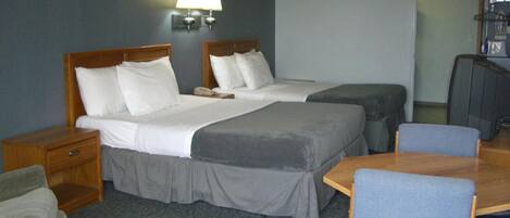 A hotel room with two beds, a desk, a chair, a TV, and a lamp.