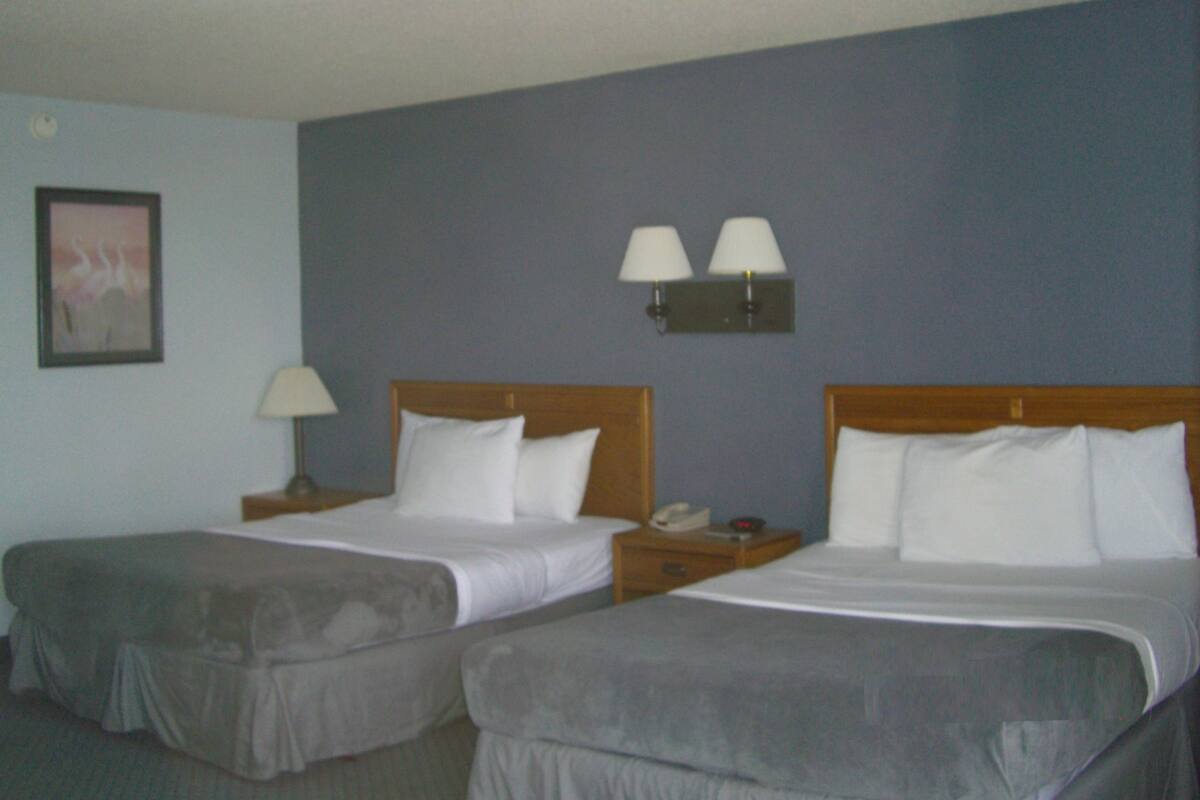 Une chambre d’hôtel avec deux lits, une table de chevet avec une lampe, une lampe fixée au mur et un tableau accroché au mur.