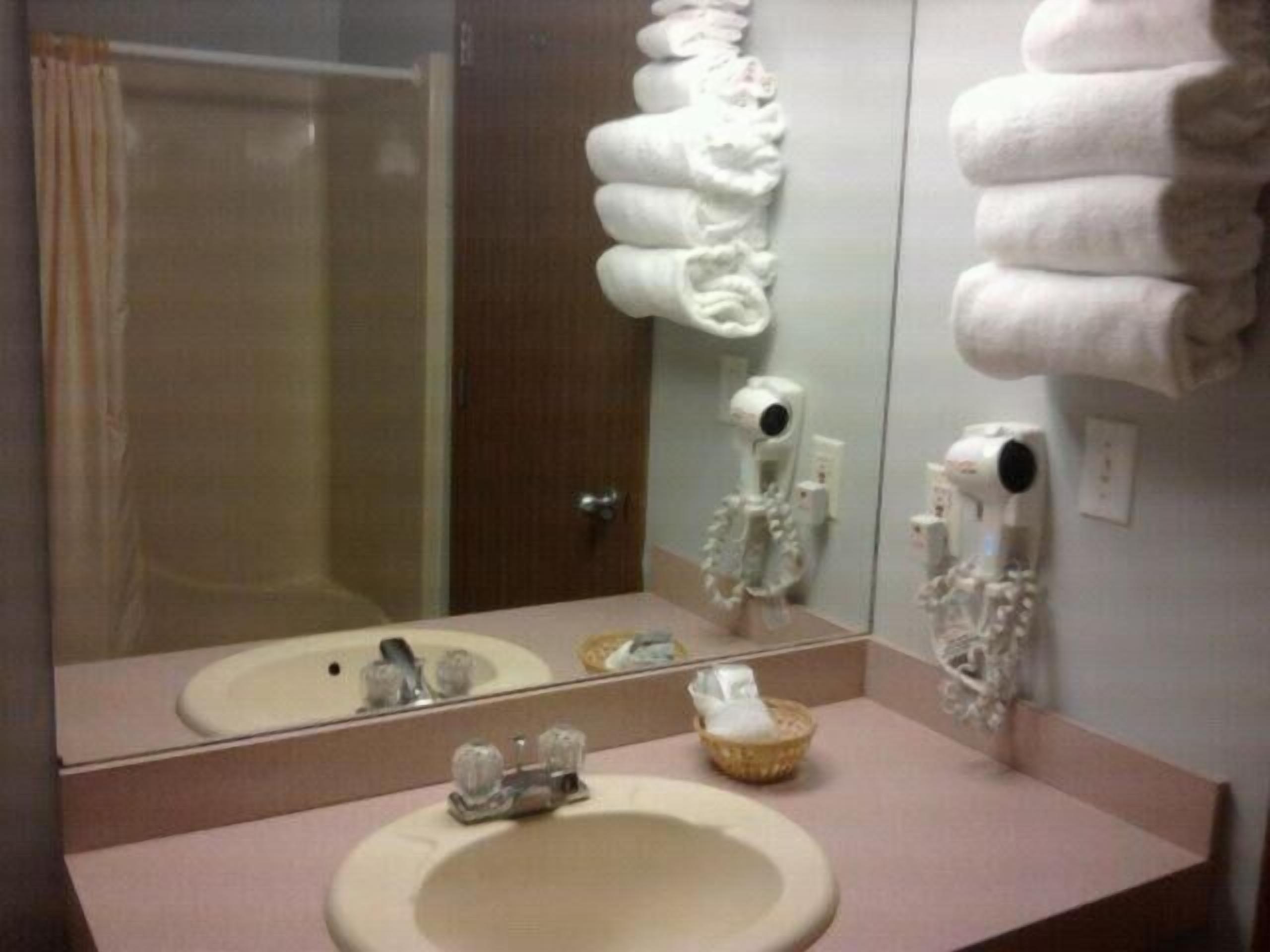 A bathroom with a sink, mirror, towel dispenser, and a shower visible through the glass door.