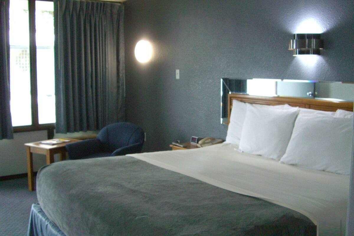 Une chambre d’hôtel avec un grand lit, un bureau, une chaise, une table de chevet avec un téléphone et une fenêtre avec des rideaux.