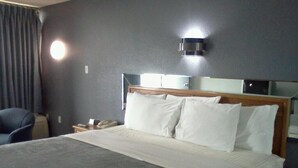 Habitación de hotel con una cama grande, una mesita de noche, una silla y una lámpara fijada a la pared.