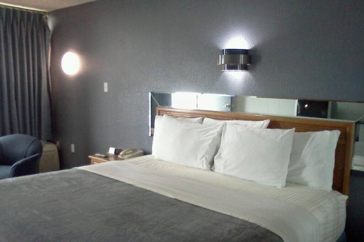 Une chambre d’hôtel avec un grand lit, une table de chevet, une chaise et un luminaire fixé au mur.