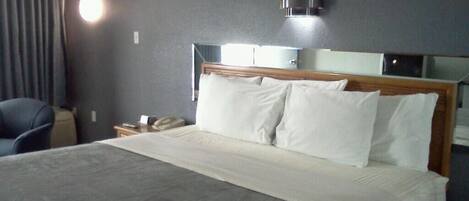 Habitación de hotel con una cama grande, una mesita de noche, una silla y una lámpara fijada a la pared.