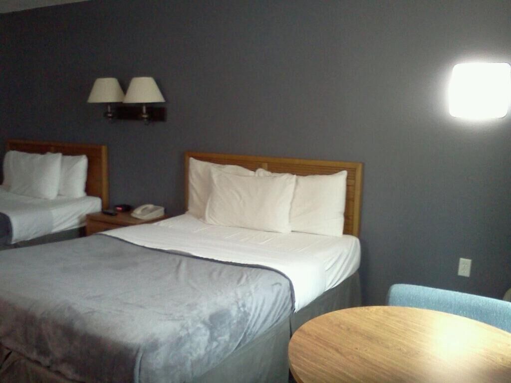 A hotel room with two single beds, a small table, and a lamp on the wall.