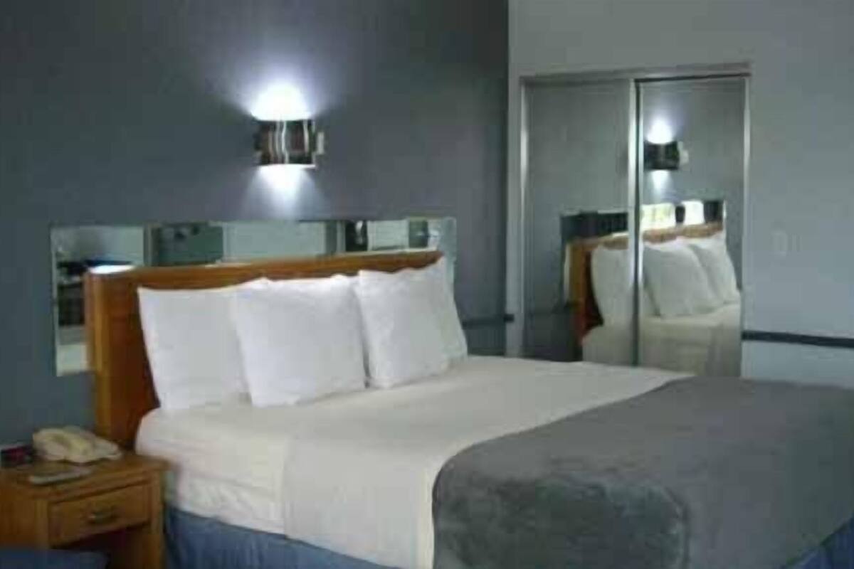 Une chambre d’hôtel avec un lit, une table de chevet, un miroir et une lampe fixée au mur.