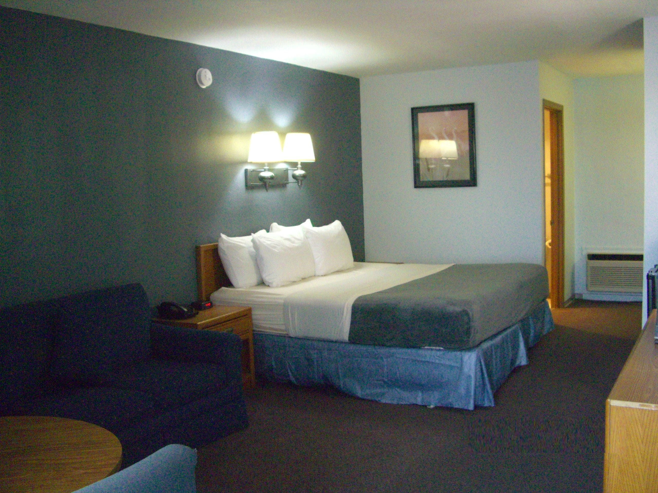 Een hotelkamer met een bed, een bureau, een stoel en een wandlamp.