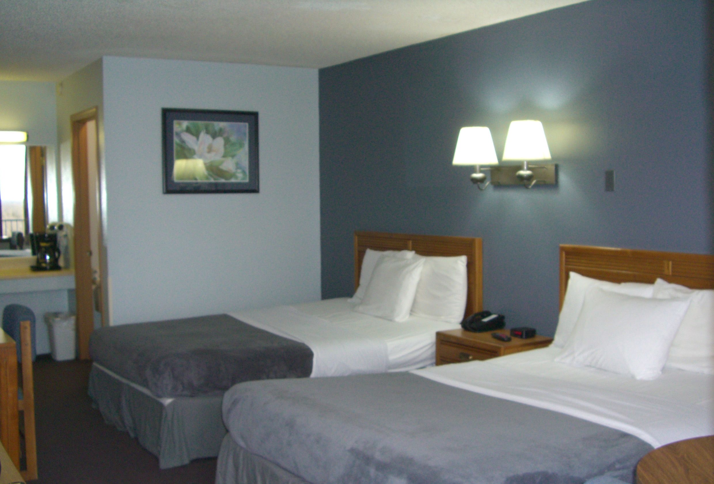 A hotel room with two single beds, a desk with a chair, a small table, a lamp, and a framed picture on the wall.
