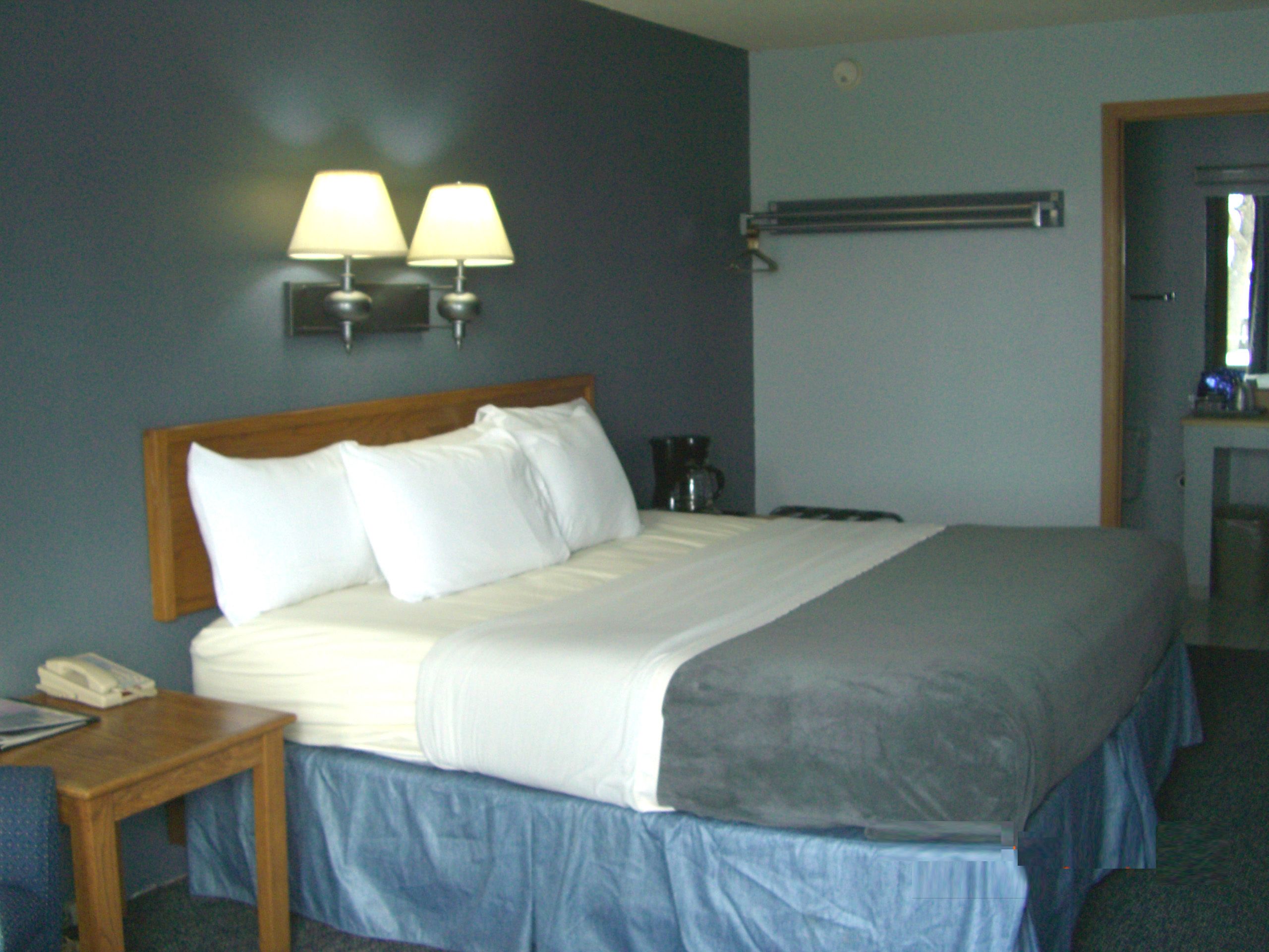 A hotel room with a large bed, a bedside table with a phone, and a lamp on the wall.