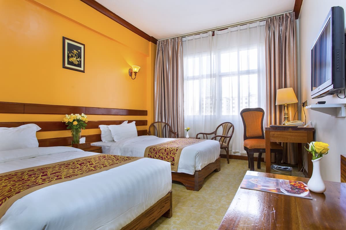 A hotel room with two beds, a desk with a lamp, a TV, and a window with curtains.
