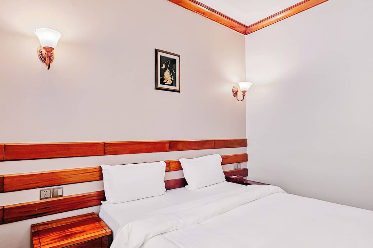 A neatly made bed with white linens, a wooden headboard, and two wall-mounted light fixtures.