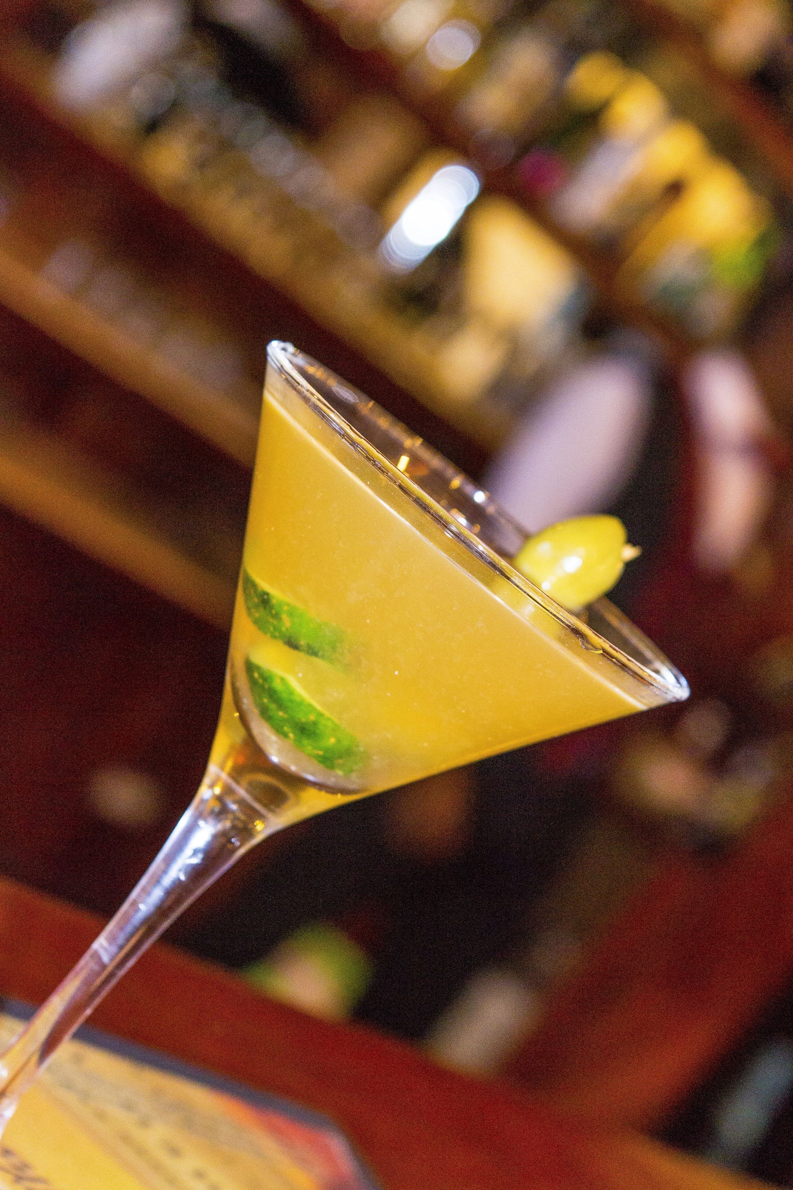 A cocktail glass with a lime wedge on a bar counter.