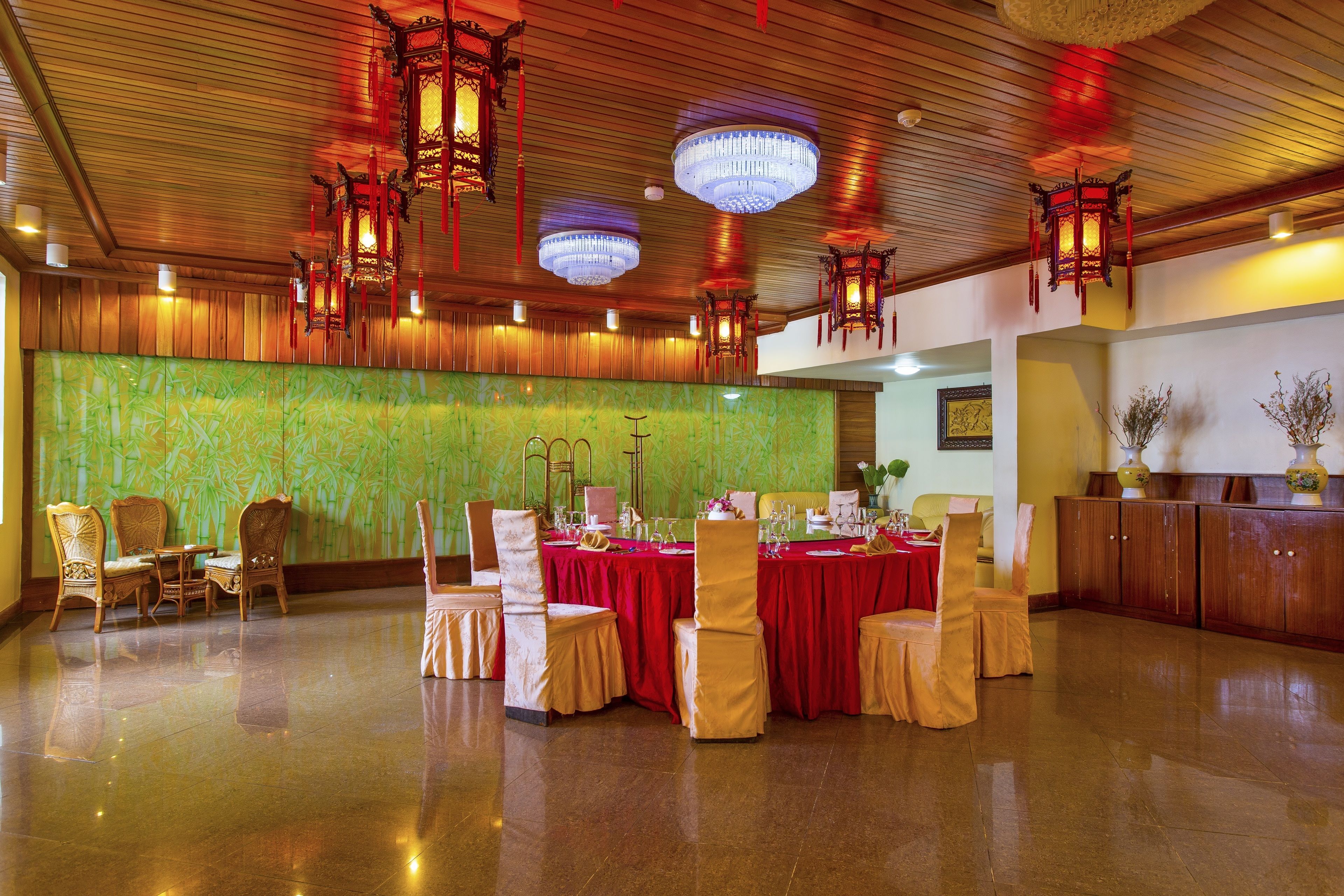A banquet hall with round tables covered in red tablecloths, wooden chairs, and traditional lanterns.