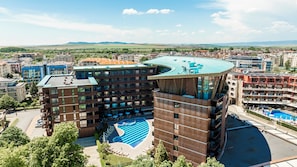 A modern hotel with a unique curved roof, a central swimming pool, and a view of the surrounding cityscape.
