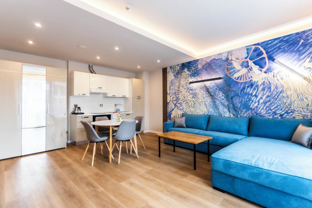 A modern living room with a blue sofa, a wooden coffee table, and a dining area with chairs and a table.