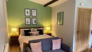 Un dormitorio con una cama, dos mesitas de noche con lámparas, un sofá gris y una puerta.