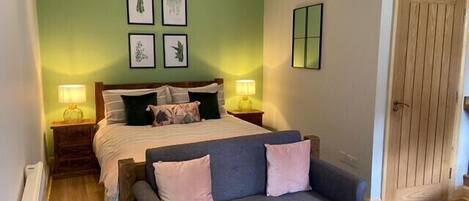 A bedroom with a bed, two bedside tables with lamps, a grey sofa, and a door.