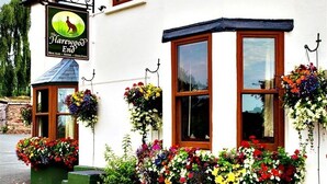 Un edificio blanco con un letrero que dice "The Harewood End" y macetas con flores alrededor de las ventanas.