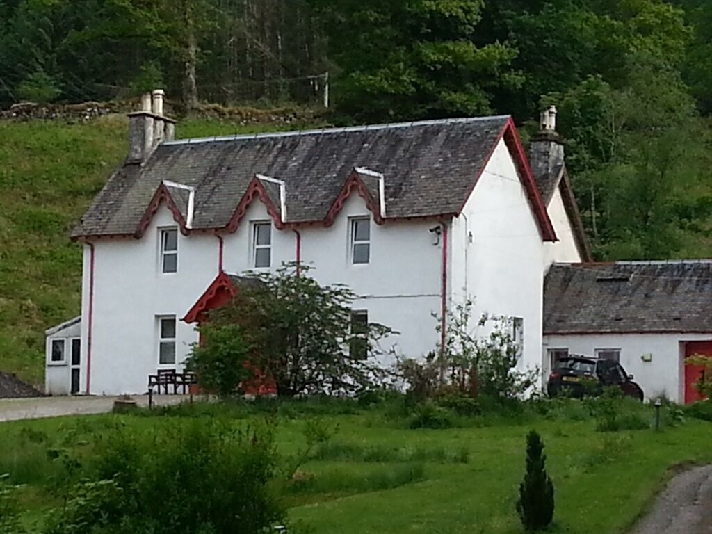 A white house with a red roof and chimney, surrounded by greenery.