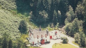 Une maison de campagne avec un toit de chaume, entourée de verdure et bordée d’un chemin sinueux.