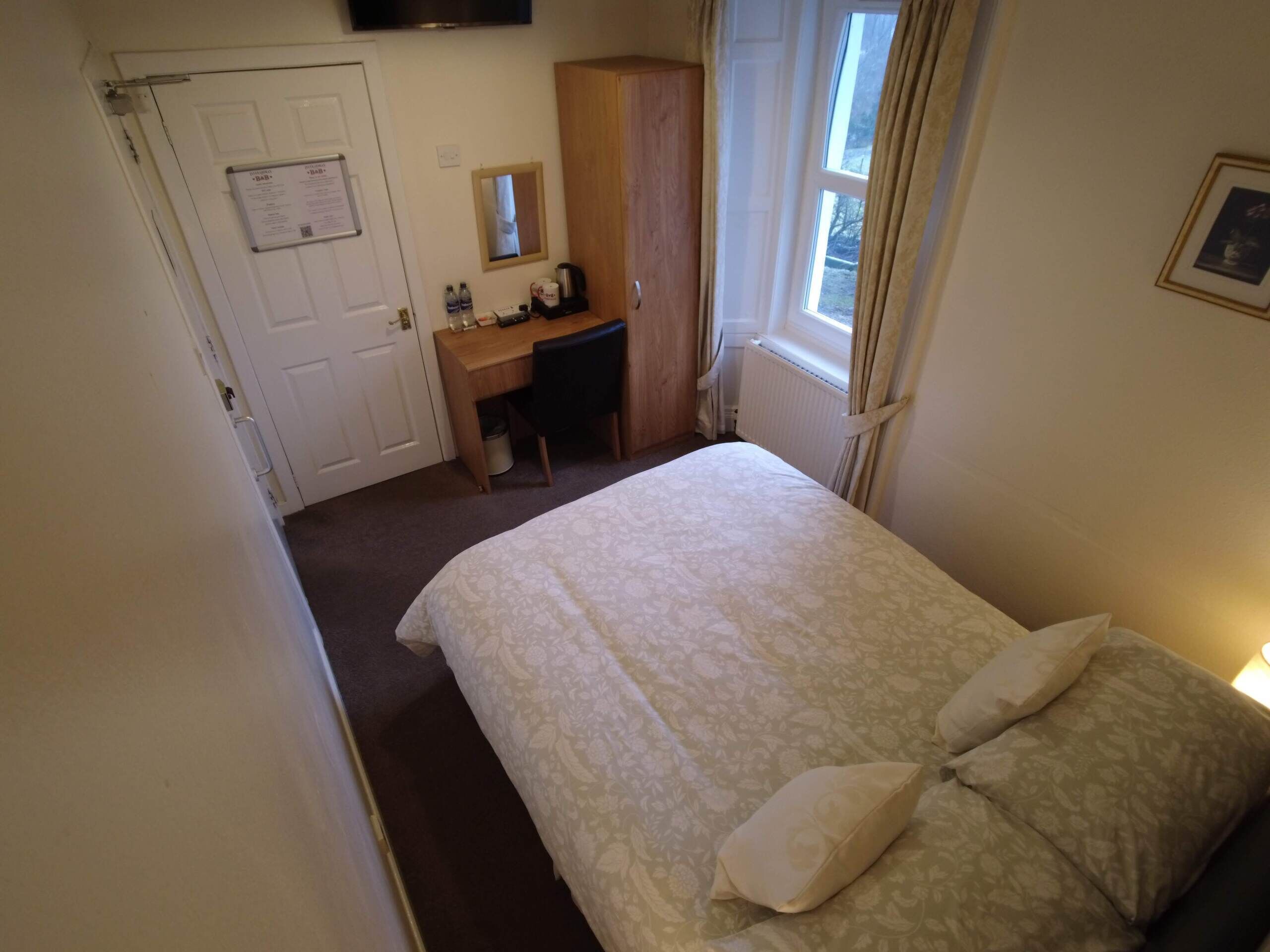 A bedroom with a bed, a desk, a wardrobe, and a window.