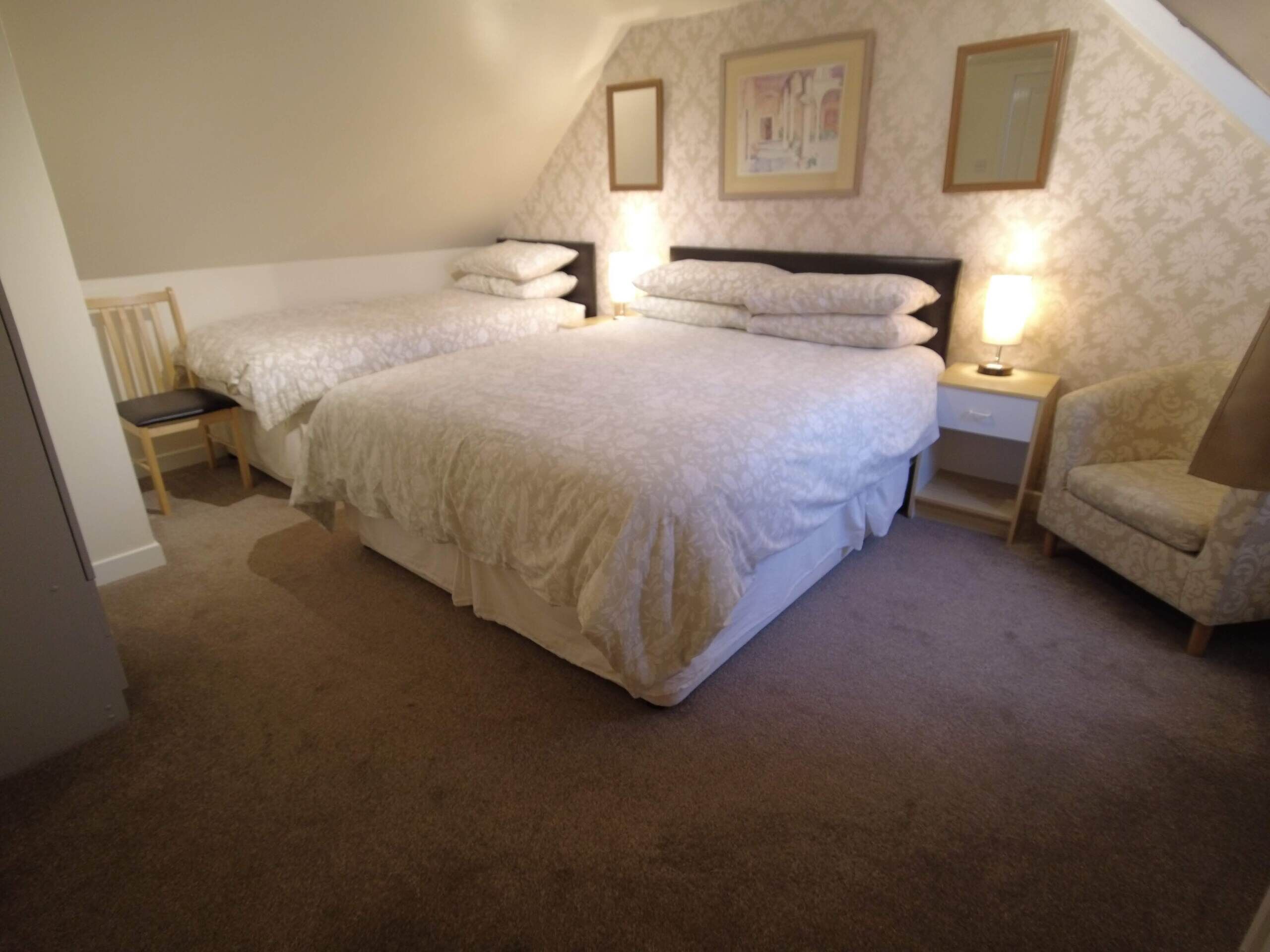 A bedroom with two single beds, a nightstand with a lamp, a chair, and a small table.