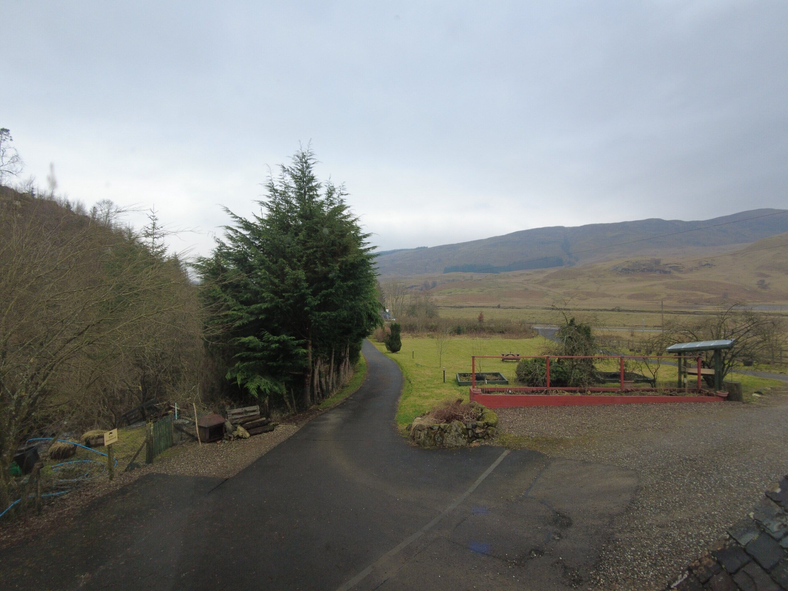 A rural road with a stone wall on one side and a grassy field on the other.