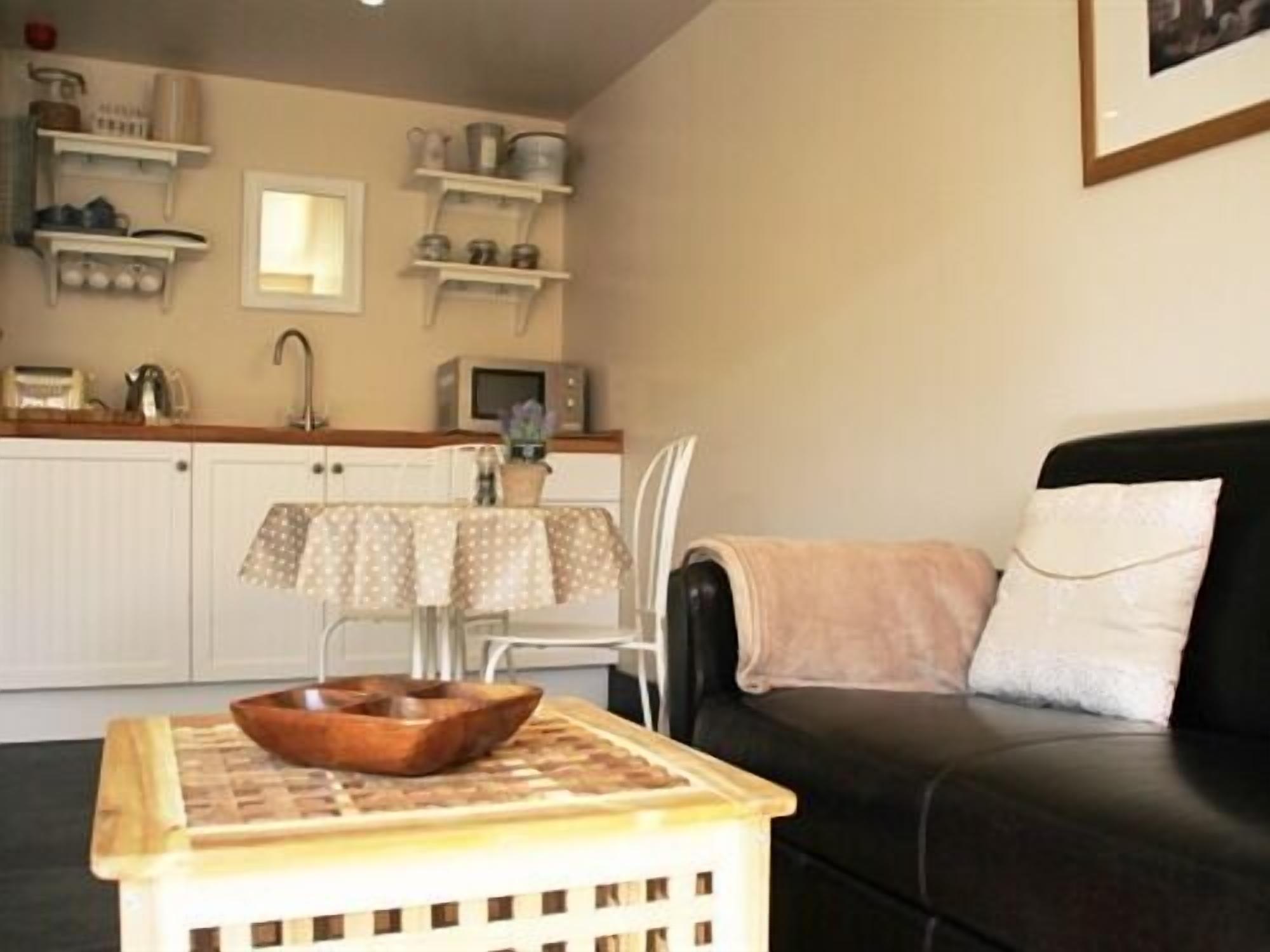 A compact living space with a kitchenette, a dining table, and a black leather sofa.
